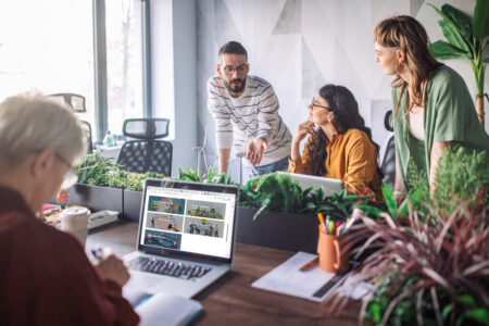People discussing around a table, computer and green plants